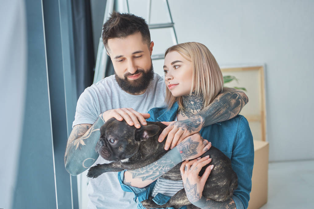 Porträt eines tätowierten Paares mit französischer Bulldogge im neuen Zuhause - Foto, Bild