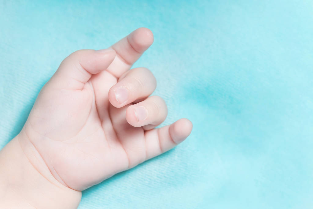 Mão de um bebê com um gesto de cabra em um fundo azul
 - Foto, Imagem