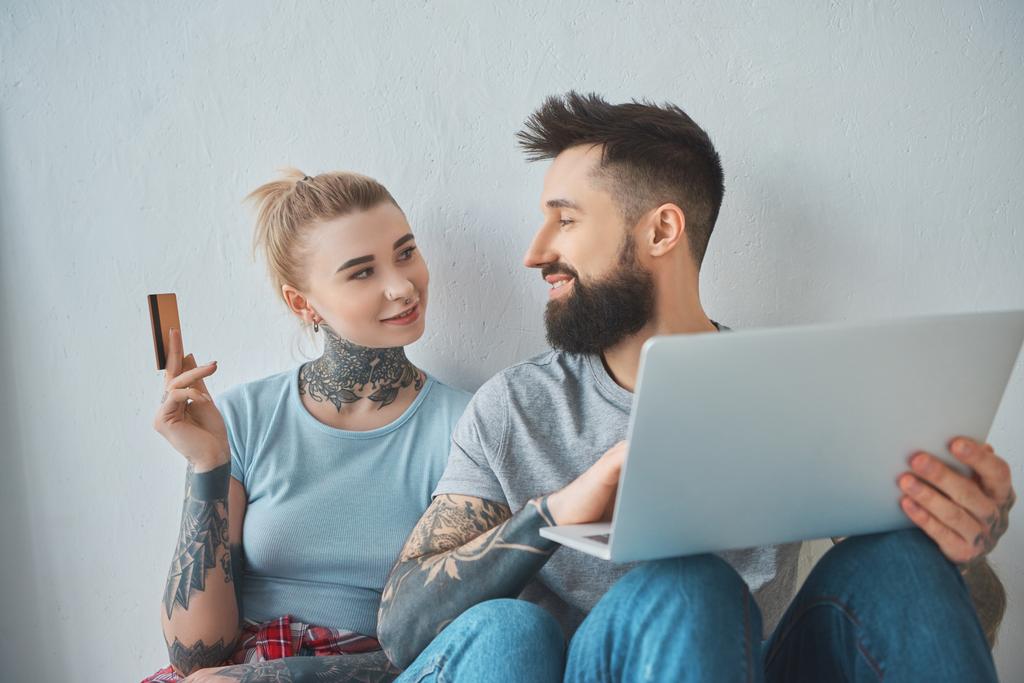 portrait of tattooed couple with laptop and credit card shopping online at new apartment - Photo, Image
