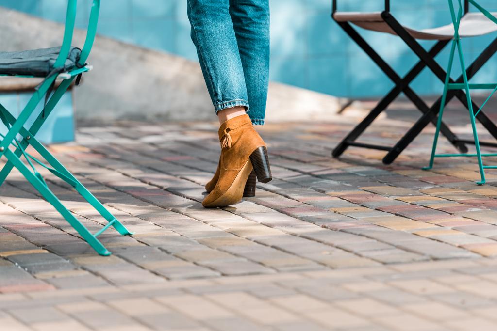 nízké část ženy na vysokých podpatcích džíny, stojící na ulici nedaleko židle do kavárny - Fotografie, Obrázek