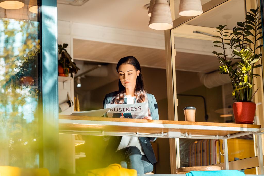 брюнетка бизнесвумен читает деловую газету в кафе с ноутбуком и кофейной чашкой
 - Фото, изображение
