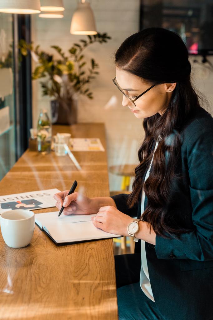 mladí teleworker psaní v planner u stolu s kávou a obchodní noviny v kavárně - Fotografie, Obrázek