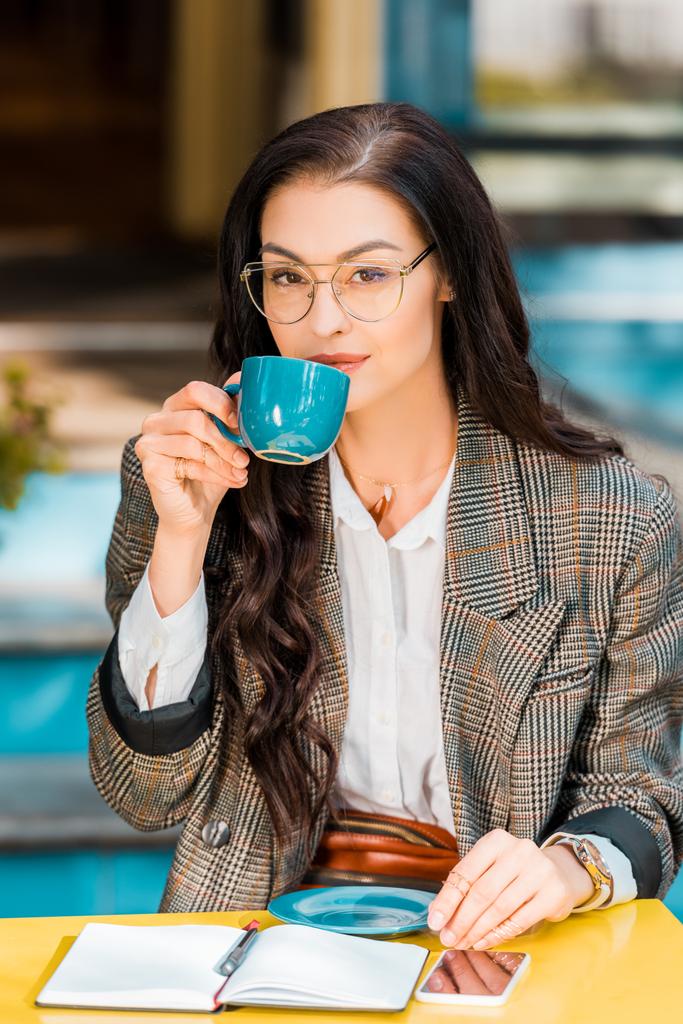 attractive woman drinking coffee on restaurant terrace with planner and smartphone - Photo, Image