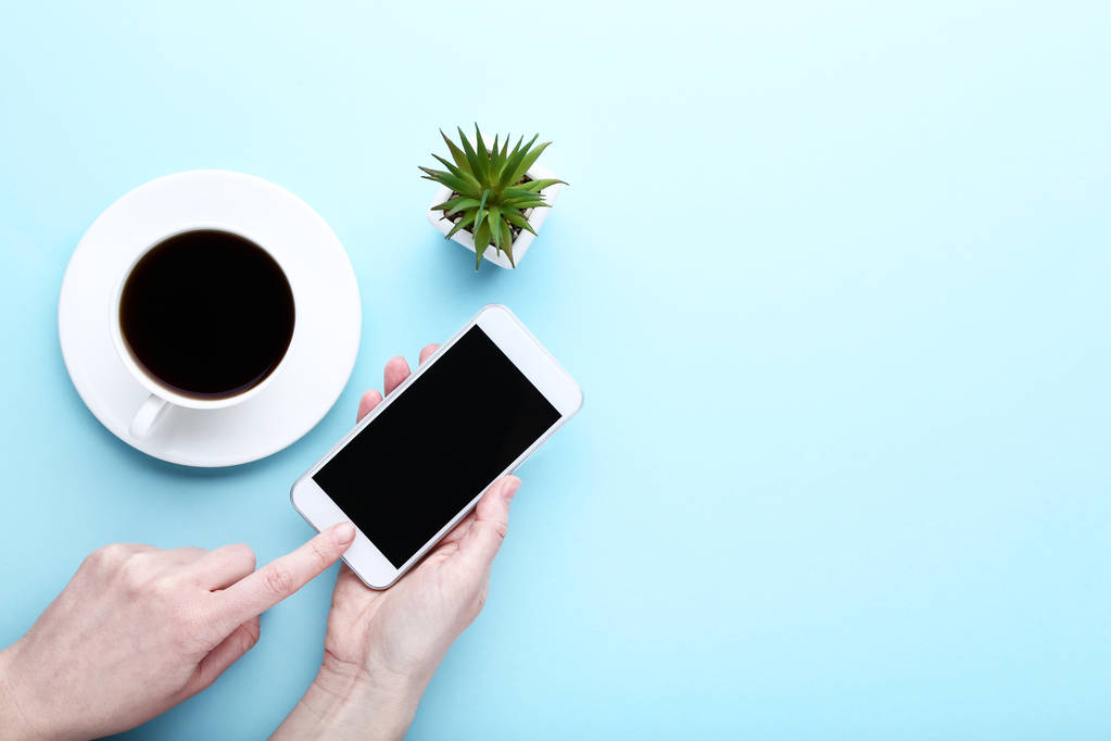 Смартфон в женских руках и чашка кофе на синем фоне
 - Фото, изображение