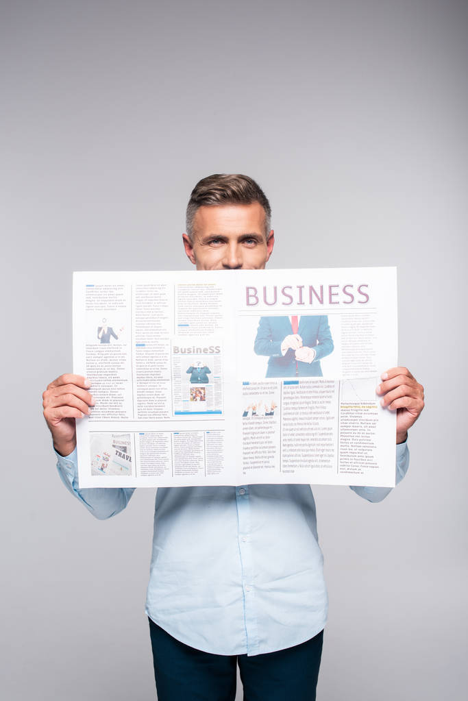 όμορφος ενήλικος επιχειρηματίας καλύπτοντας πρόσωπο με επιχειρηματική εφημερίδα απομονωθεί σε λευκό - Φωτογραφία, εικόνα