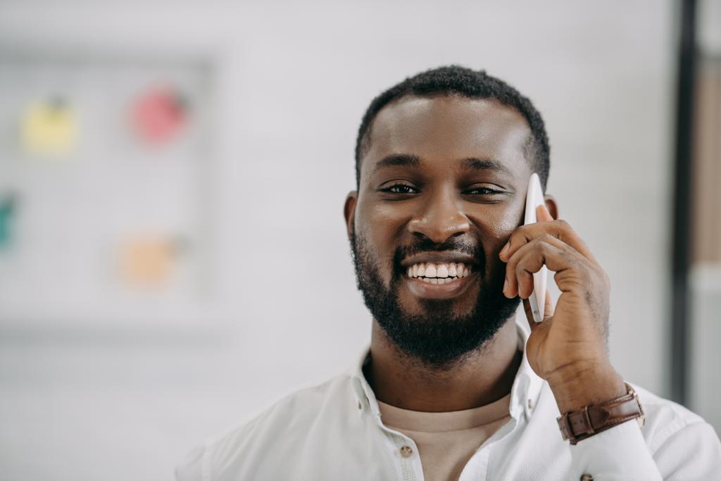 オフィスでスマート フォンで話す笑顔のハンサムなアフリカ系アメリカ人実業家の肖像画 - 写真・画像