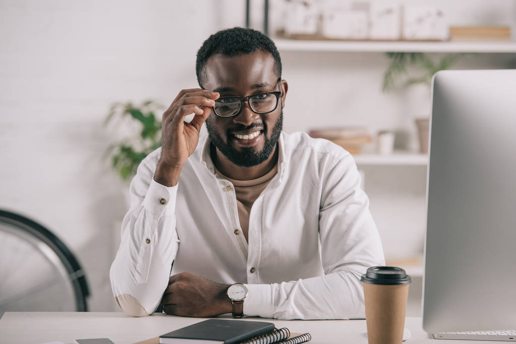 sorridente bell'uomo d'affari africano americano che tocca gli occhiali in ufficio
 - Foto, immagini