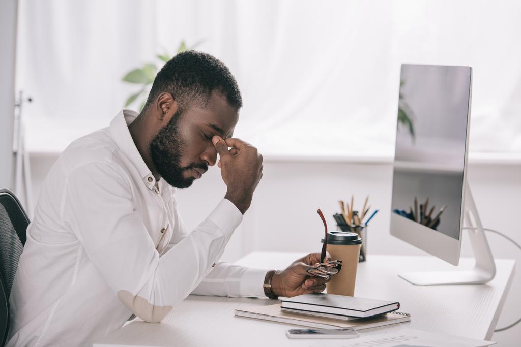 вид збоку втомлений афроамериканський бізнесмен торкається моста носа за столом з комп'ютером в офісі
 - Фото, зображення