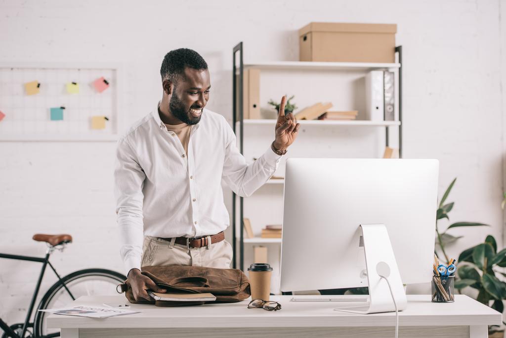 fröhlich gutaussehender afrikanisch-amerikanischer Geschäftsmann zeigt im Büro nach oben und schaut auf den Computer - Foto, Bild