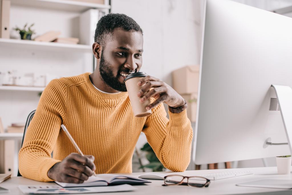 コーヒーを飲み、オフィスでノートに描くオレンジのセーターでハンサムなアフリカ系アメリカ人デザイナー - 写真・画像