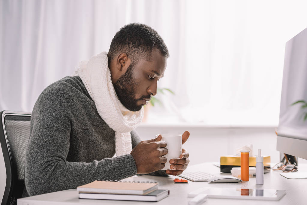 homme afro-américain malade avec tasse de boisson chaude et des médicaments assis sur le lieu de travail
 - Photo, image