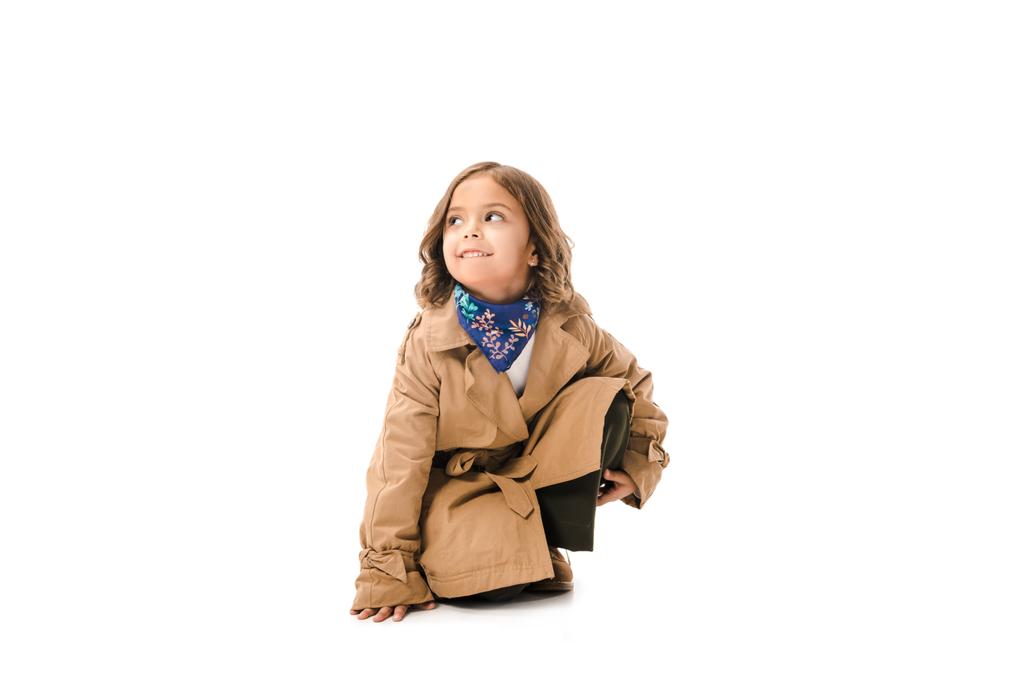criança elegante em casaco de trincheira sentado no chão isolado no branco
 - Foto, Imagem