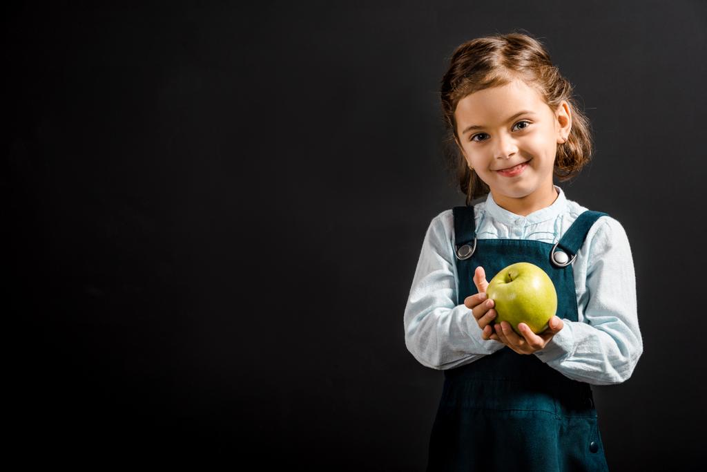 portrait of smiling schoolgirl with apple in hands isolated on black - Photo, Image