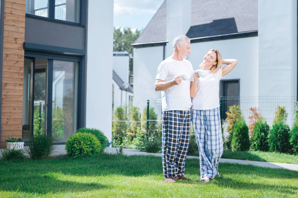 Esposa radiante y esposo usando pantalones de pijama cuadrados y zapatos de casa
 - Foto, Imagen