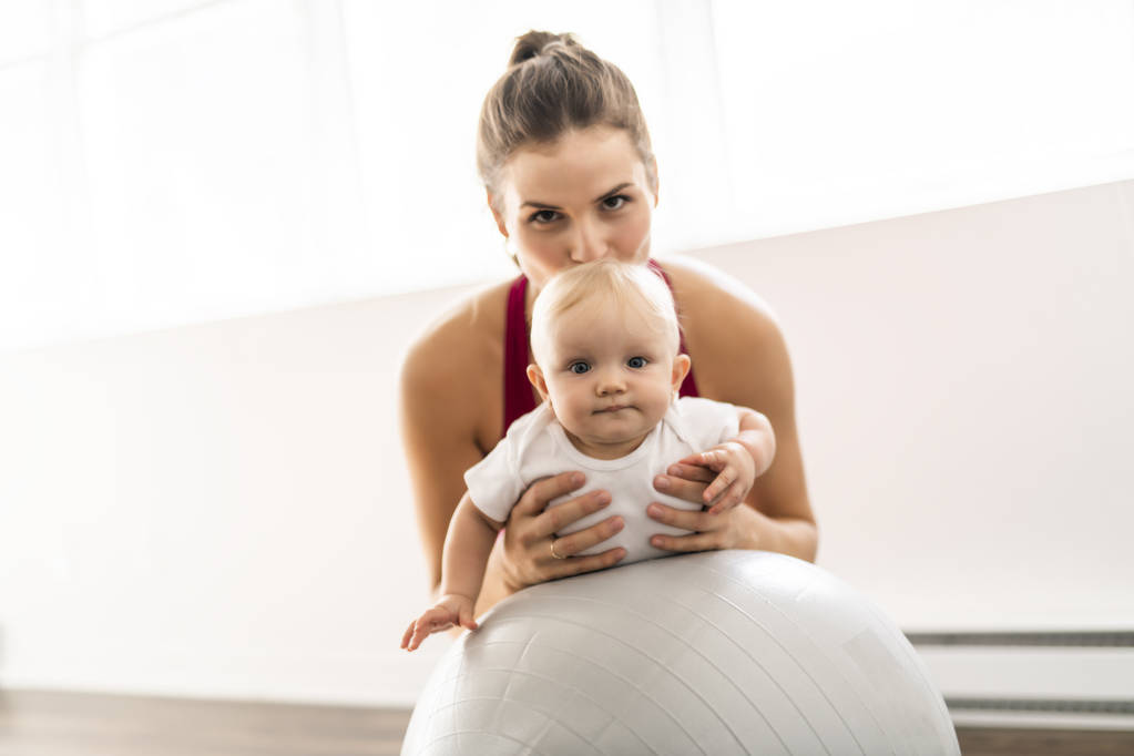 Портрет красивой молодой матери в спортивной одежде со своим очаровательным малышом на тренировке
 - Фото, изображение