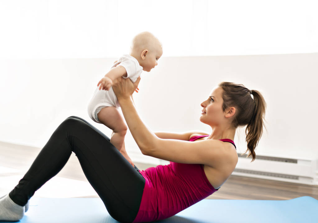 Muotokuva kaunis nuori äiti urheiluvaatteissa hänen viehättävä pieni vauva harjoitteluun
 - Valokuva, kuva
