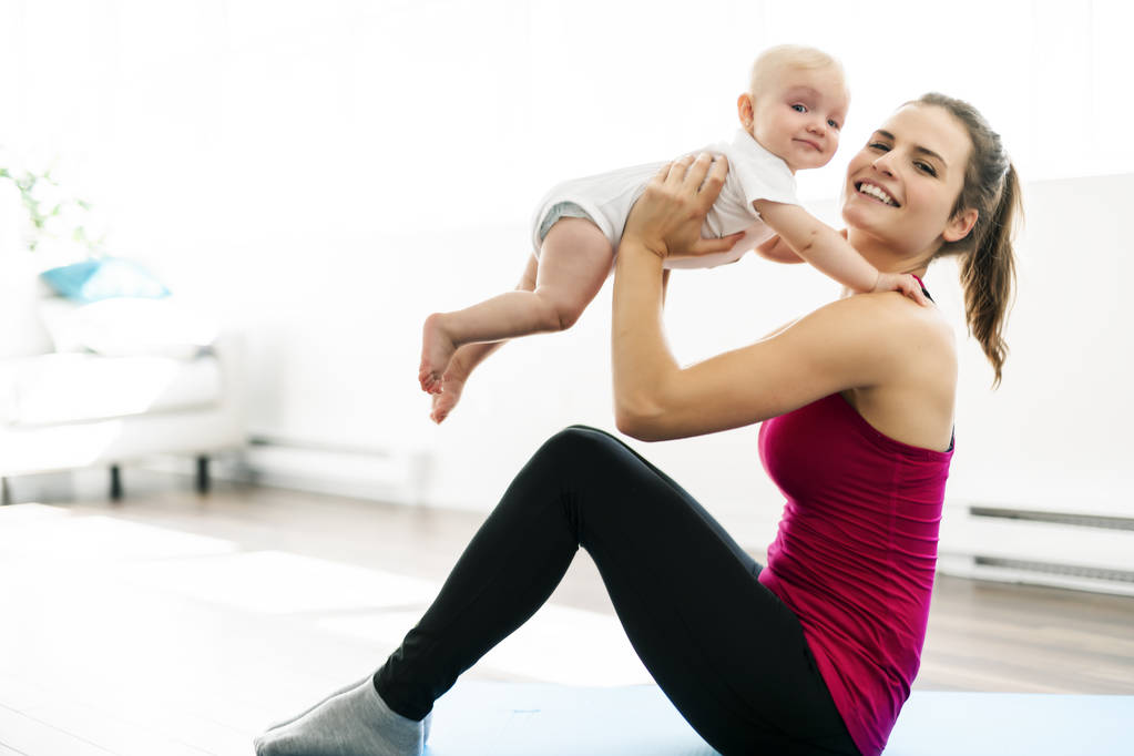 Um retrato de bela jovem mãe em roupas esportivas com seu pequeno bebê encantador em sessão de treinamento
 - Foto, Imagem