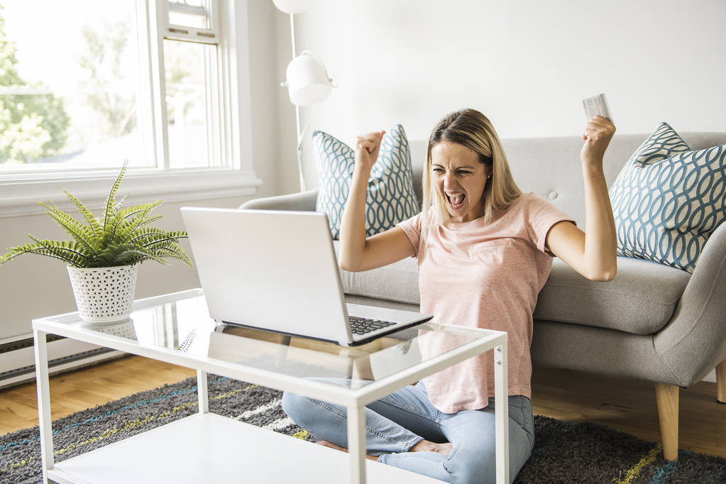 Mujer feliz con una tarjeta de crédito y un ordenador portátil en el sofá en casa - Foto, imagen