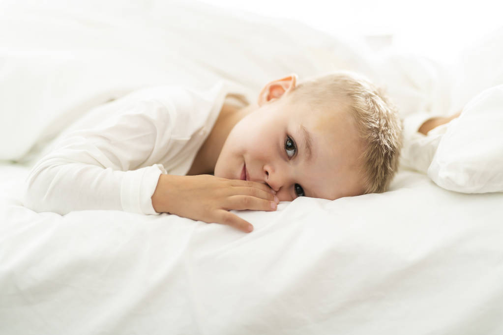 χαριτωμένο τεσσάρων ετών αγόρι σε λευκά κλινοσκεπάσματα - Φωτογραφία, εικόνα