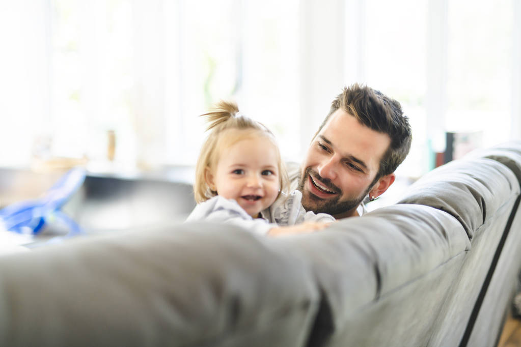 Junger Vater mit kleiner Tochter auf Sofa zu Hause - Foto, Bild