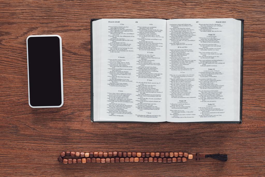 a fából készült asztal megnyitott Szent Biblia, gyöngyök és smartphone felső nézetében - Fotó, kép