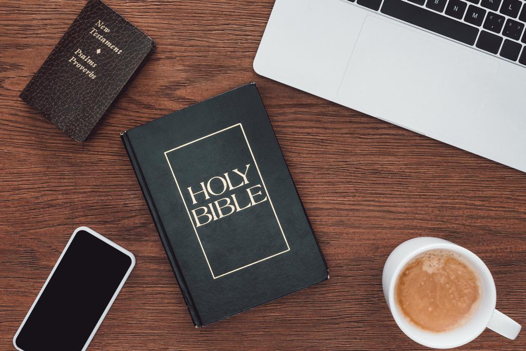 bovenaanzicht van Heilige Bijbel met nieuwe testament, gadgets en koffie op de houten tafel - Foto, afbeelding