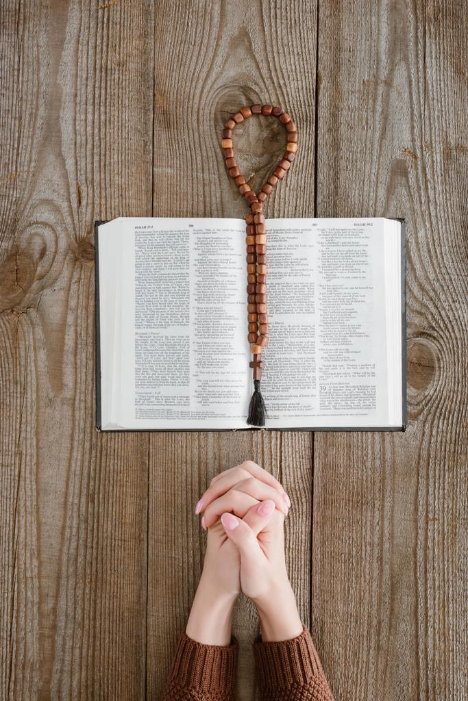 recortado disparo de la mujer rezando con la Biblia y perlas sagradas en la mesa de madera
 - Foto, Imagen