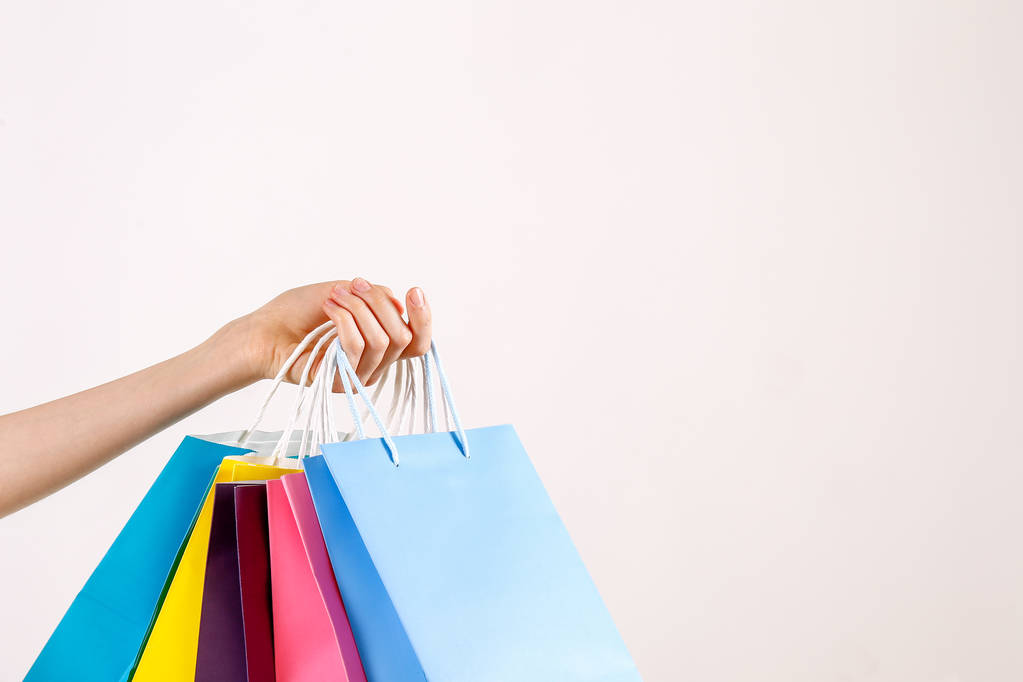 Cropped shot of female hand holding bunch of different colorful blank shopping bags over isolated white background. Many packets with in woman's arms. Black friday sale concept. Copy space, close up. - Photo, Image
