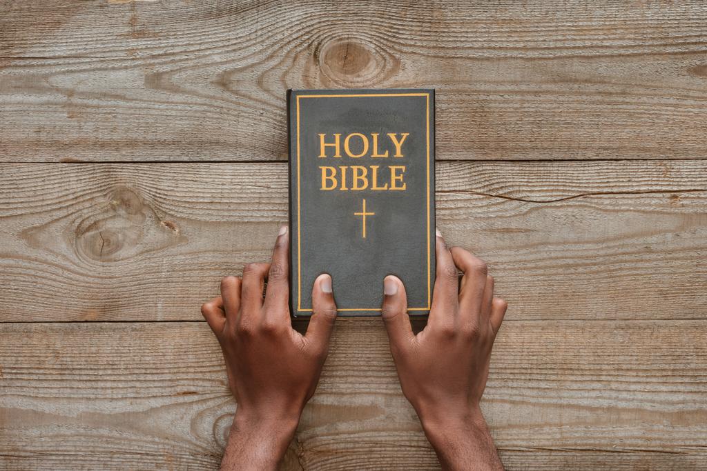 cropped shot of man holding holy bible on rustic wooden table - Photo, Image