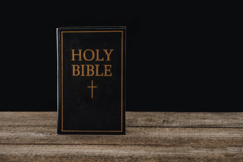 primer plano plano de la sagrada biblia de pie sobre una mesa de madera aislada en negro
 - Foto, Imagen