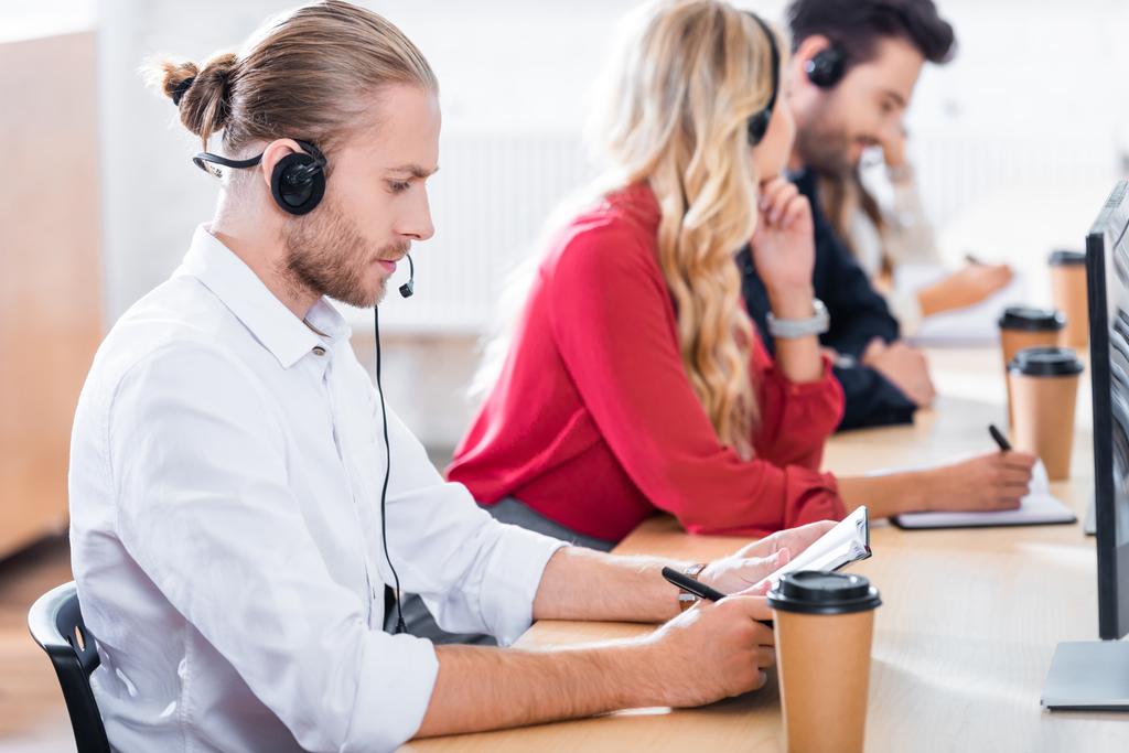 selectieve aandacht van call center exploitanten in hoofdtelefoons met laptops werken bij werkplek op kantoor - Foto, afbeelding