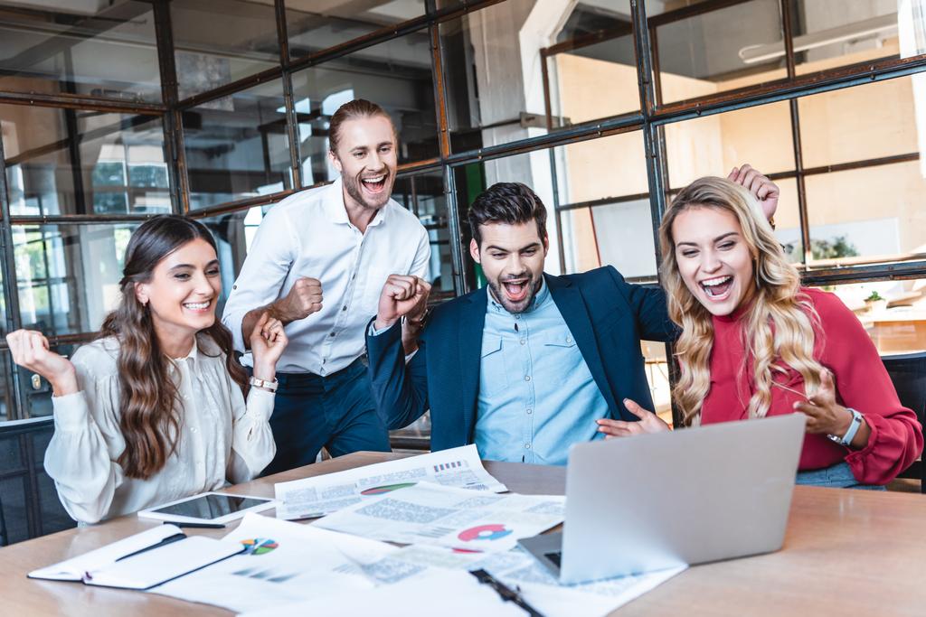 счастливый успешной бизнес-команды, глядя на экран ноутбука на рабочем месте в офисе
  - Фото, изображение