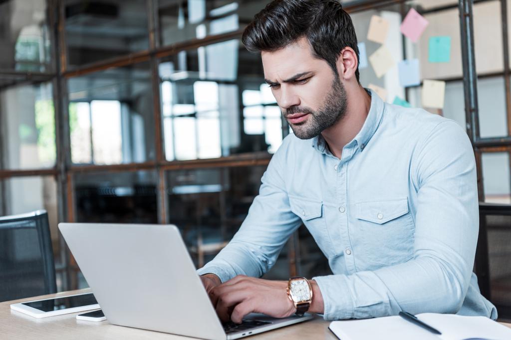 зосереджений молодий бізнесмен використовує ноутбук на робочому місці
 - Фото, зображення