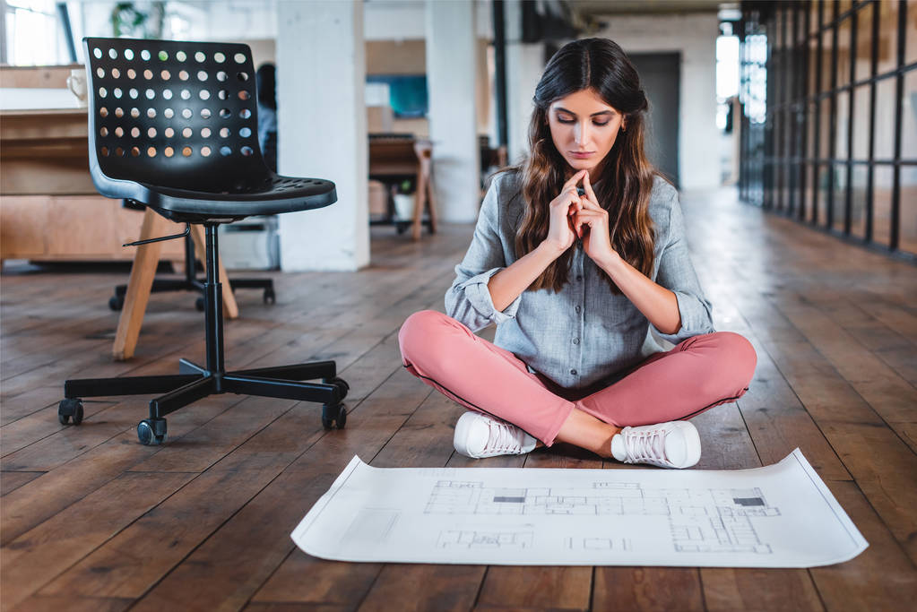 сконцентрированная молодая предпринимательница, сидящая в позе лотоса и работающая с документами в офисе
 - Фото, изображение