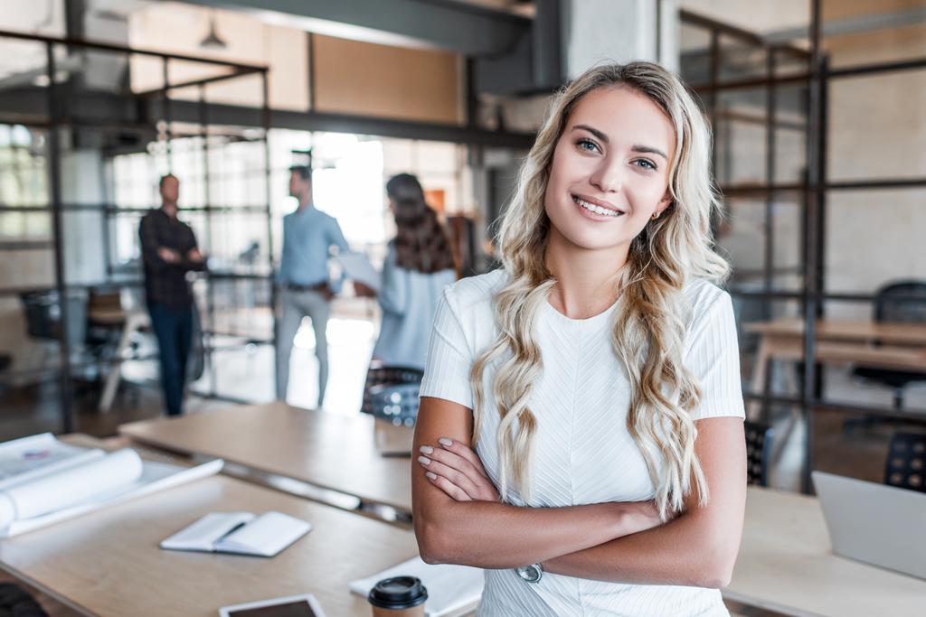 красивая молодая деловая женщина, стоящая со скрещенными руками и улыбающаяся в офисе перед камерой
 - Фото, изображение