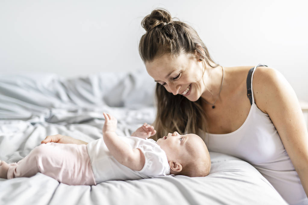 Portrait of a beautiful mother with her 2 month old baby in the bedroom - Photo, Image