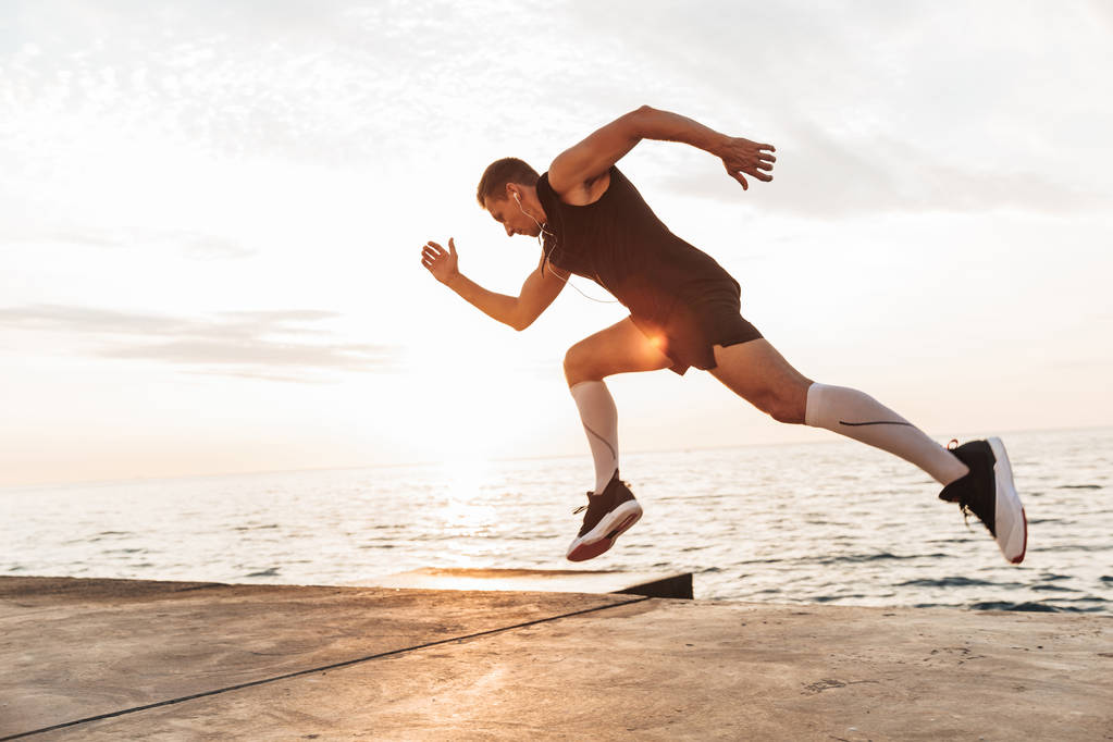 Образ красивого сильного молодого спортсмена, бегущего на открытом воздухе на пляже
. - Фото, изображение