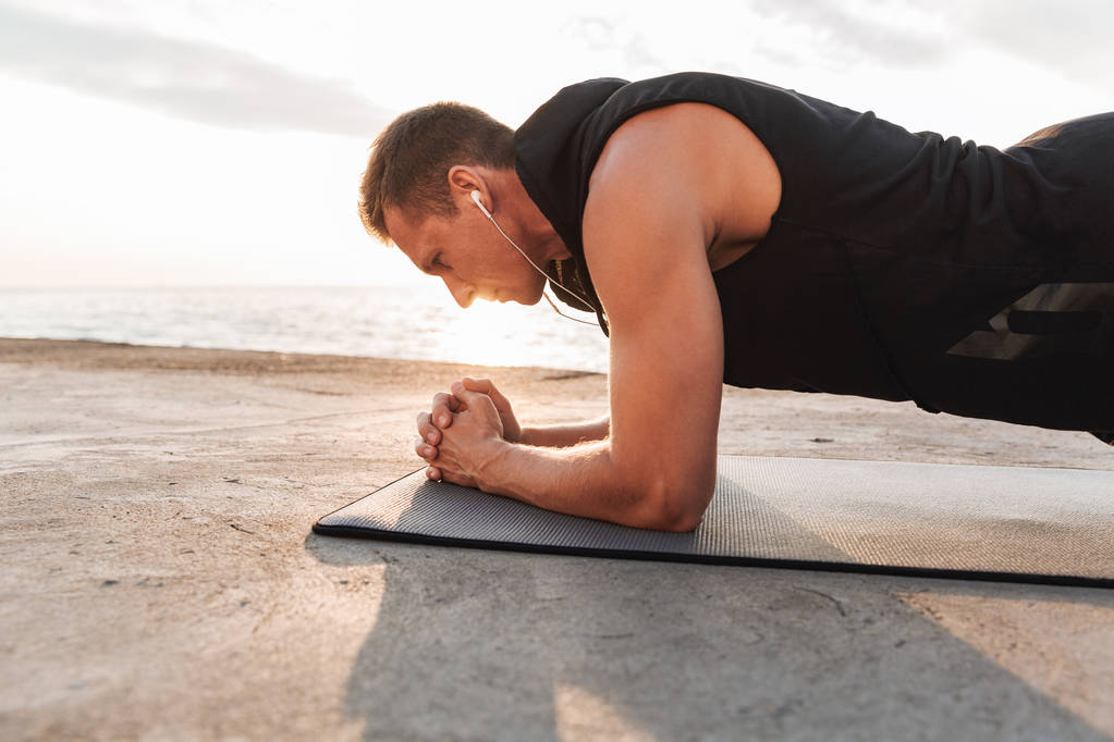 Foto de un joven deportista fuerte al aire libre en la playa hacer ejercicios deportivos escuchando música
. - Foto, imagen