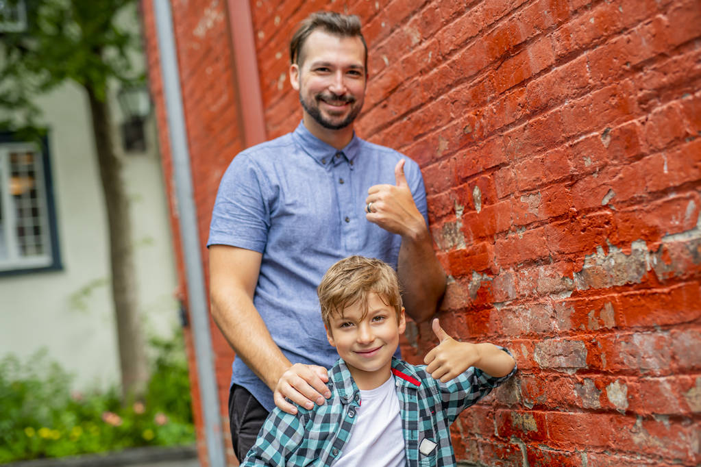 Adorable lindo chico staing cerca de una pared de ladrillo rojo con su padre
 - Foto, Imagen
