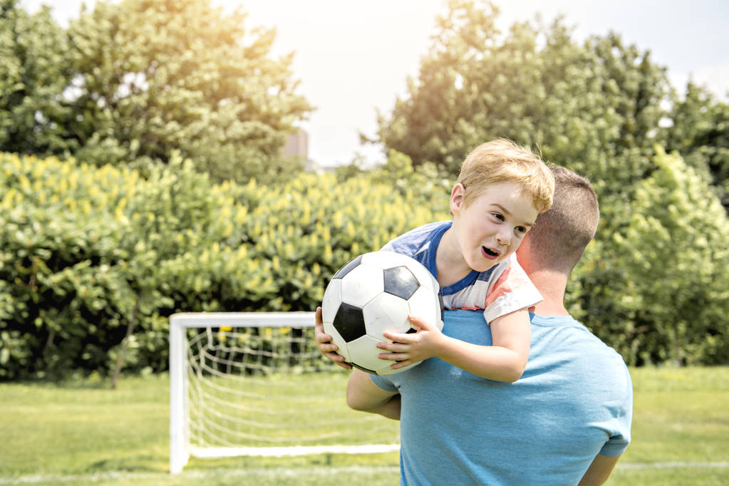 Mężczyzna z dzieckiem gra w piłkę nożną na boisku - Zdjęcie, obraz