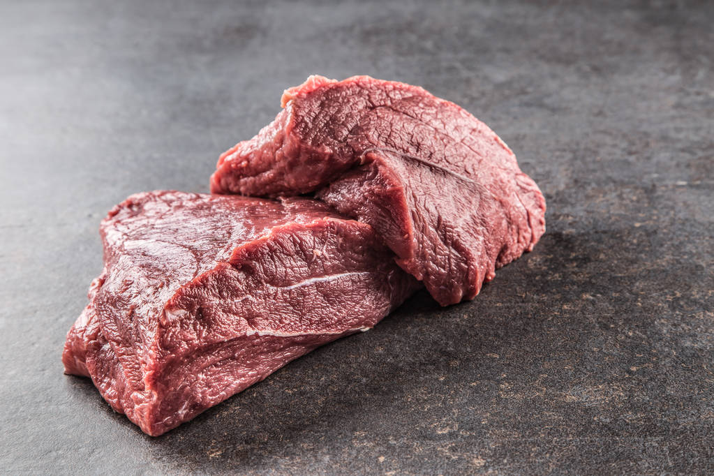 Portion of raw beef shoulder on dark butcher board. - Photo, Image
