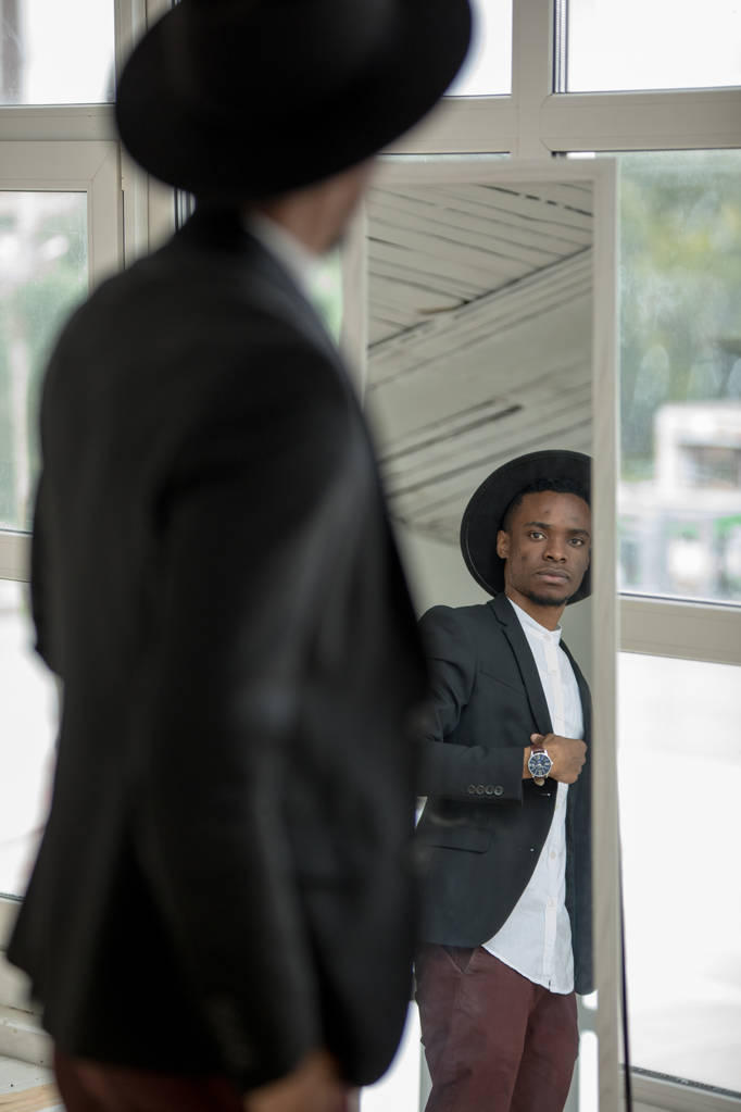 African American mężczyzna w kapeluszu patrzy w lustro. - Zdjęcie, obraz
