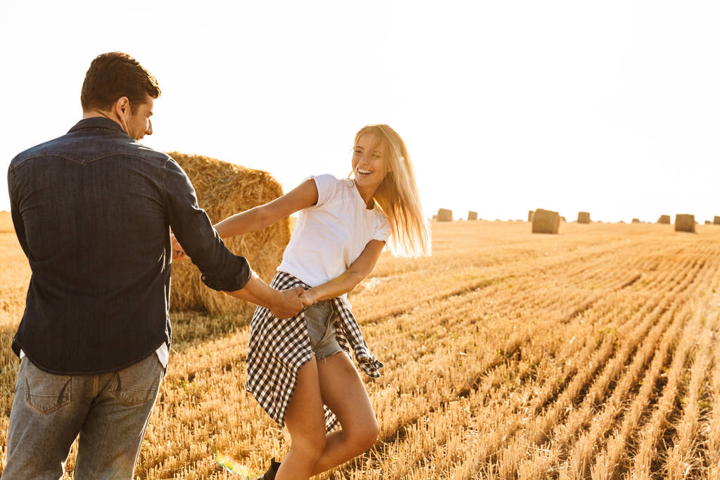 Foto von schönen Paar Mann und Frau Spaß beim Spaziergang durch goldenes Feld mit Heuhaufen bei sonnigem Tag - Foto, Bild