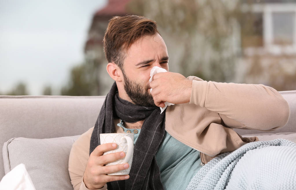 Beteg ember csésze forró teát köhög, otthon a kanapén - Fotó, kép
