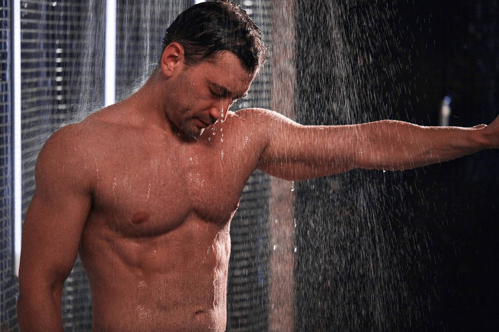 Hombre guapo tomando una ducha, refrescándose después de un día de trabajo caliente
. - Foto, imagen