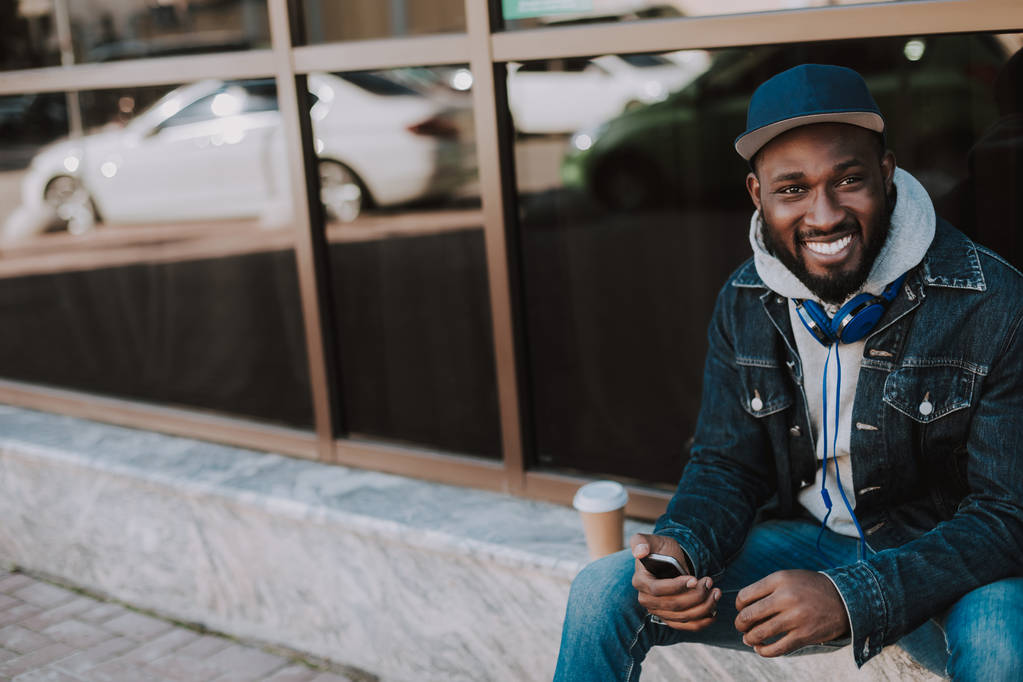 Radosny afro amerykański facet siedzi w przestrzeni miejskiej - Zdjęcie, obraz