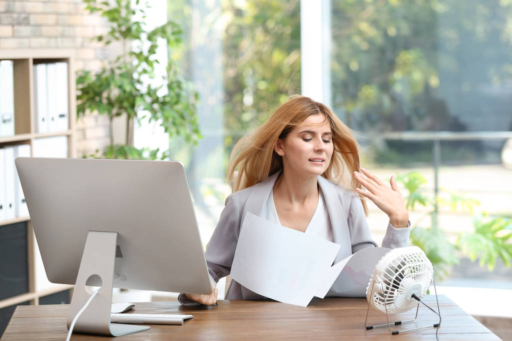 Businesswoman suffering from heat in front of small fan at workplace - Photo, Image