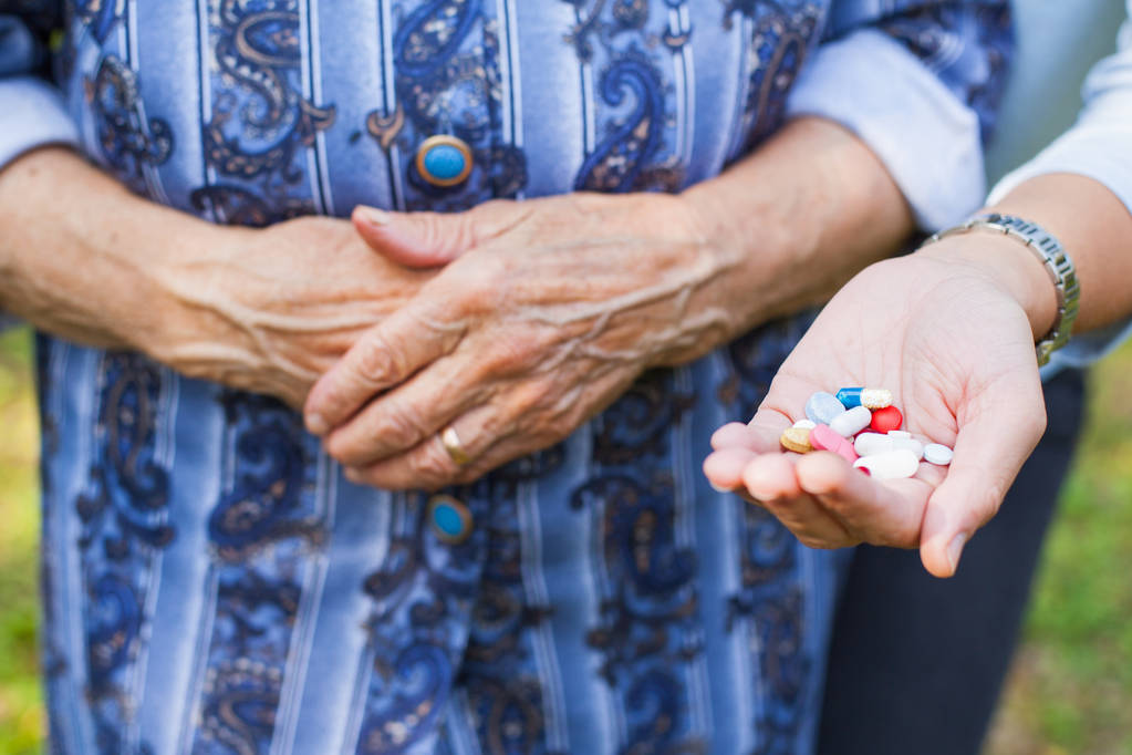 Közelkép kép ráncos idős kéz és egy maroknyi gyógyszerek és vitaminok - Fotó, kép