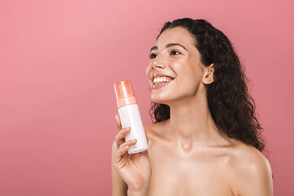 Ritratto di felice sorridente bella giovane donna posa isolata su sfondo rosa prendersi cura della sua pelle in possesso di cosmetici
. - Foto, immagini