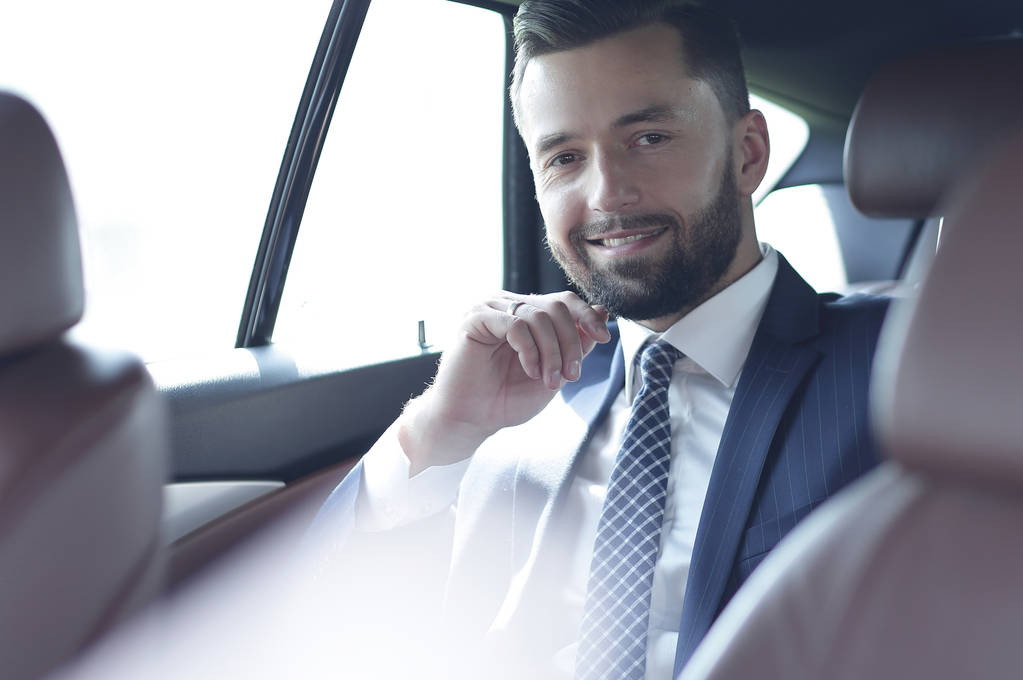 Hombre de negocios sonriente sentado en el asiento trasero de un coche
 - Foto, Imagen